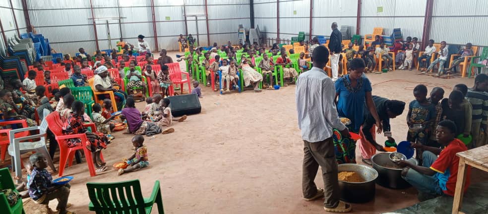 Children gathered in community hall receiving meals and support